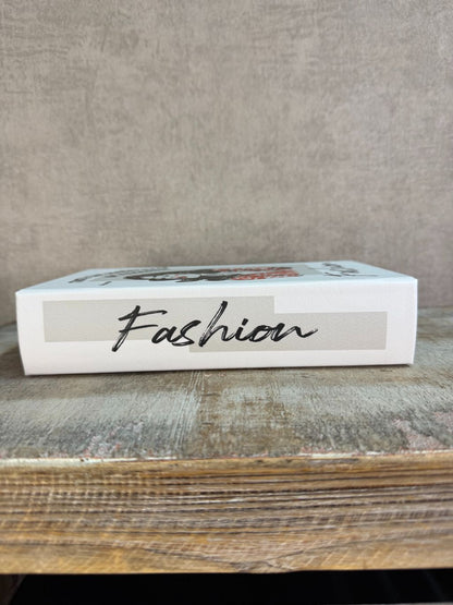 Wit opbergboek Fashion met illustratie en tekst op de voorkant, staand op een houten ondergrond.