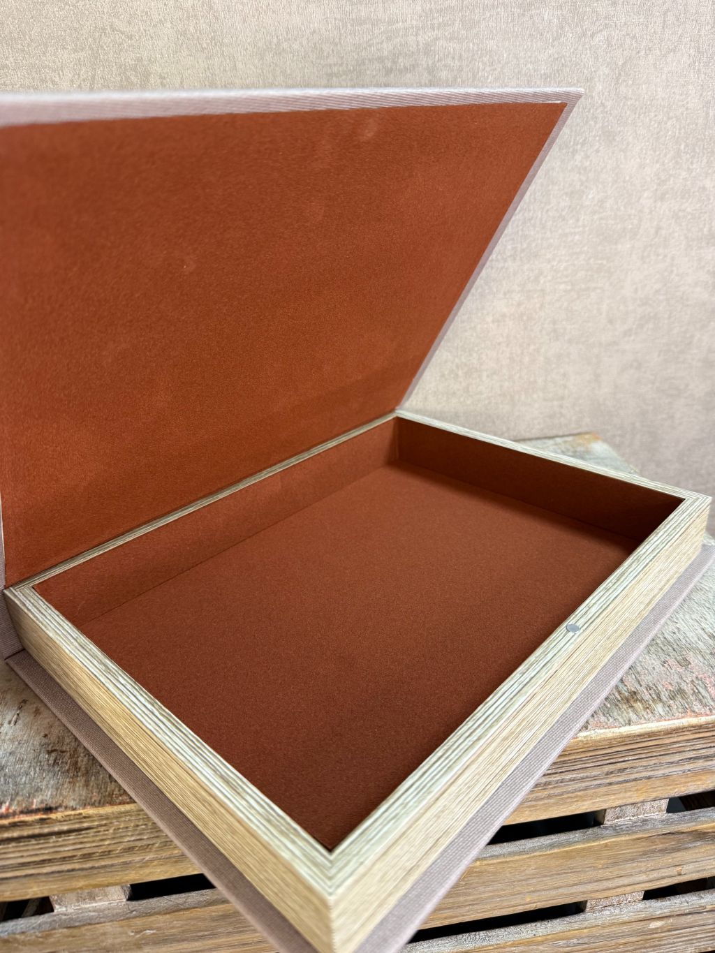 Taupekleurig opbergboek Less is More met witte tekst, liggend op een houten ondergrond.