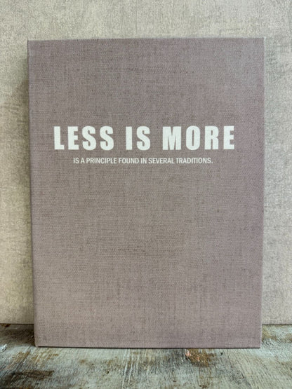 Taupekleurig opbergboek Less is More met witte tekst, liggend op een houten ondergrond.