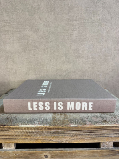 Taupekleurig opbergboek Less is More met witte tekst, liggend op een houten ondergrond.