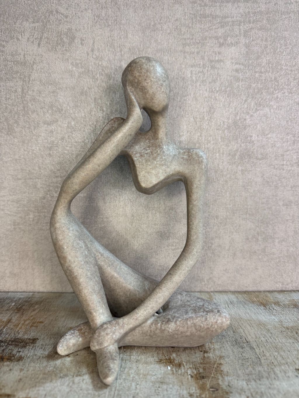 Abstract ornament van een zittend figuur in beige-grijze tint op een houten ondergrond.