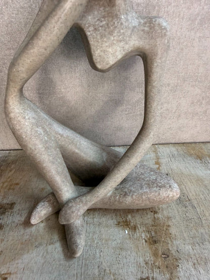 Abstract ornament van een zittend figuur in beige-grijze tint op een houten ondergrond.