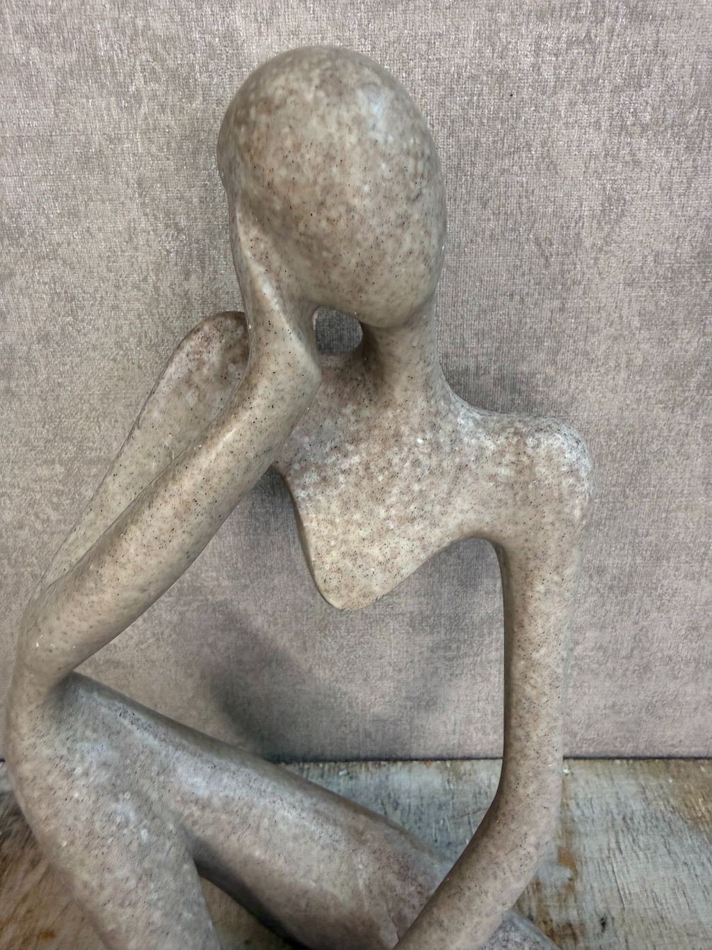 Abstract ornament van een zittend figuur in beige-grijze tint op een houten ondergrond.