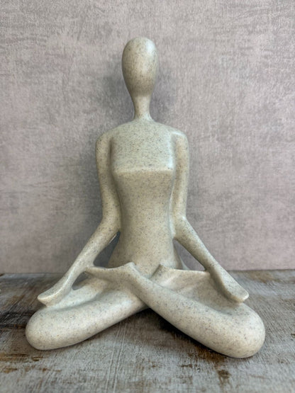 Ornament van een zittend figuur in lotuspositie in beige-grijze kleur op een houten ondergrond.