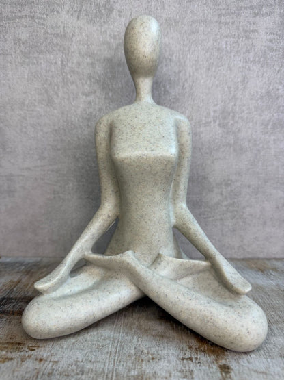 Ornament van een zittend figuur in lotuspositie in beige-grijze kleur op een houten ondergrond.