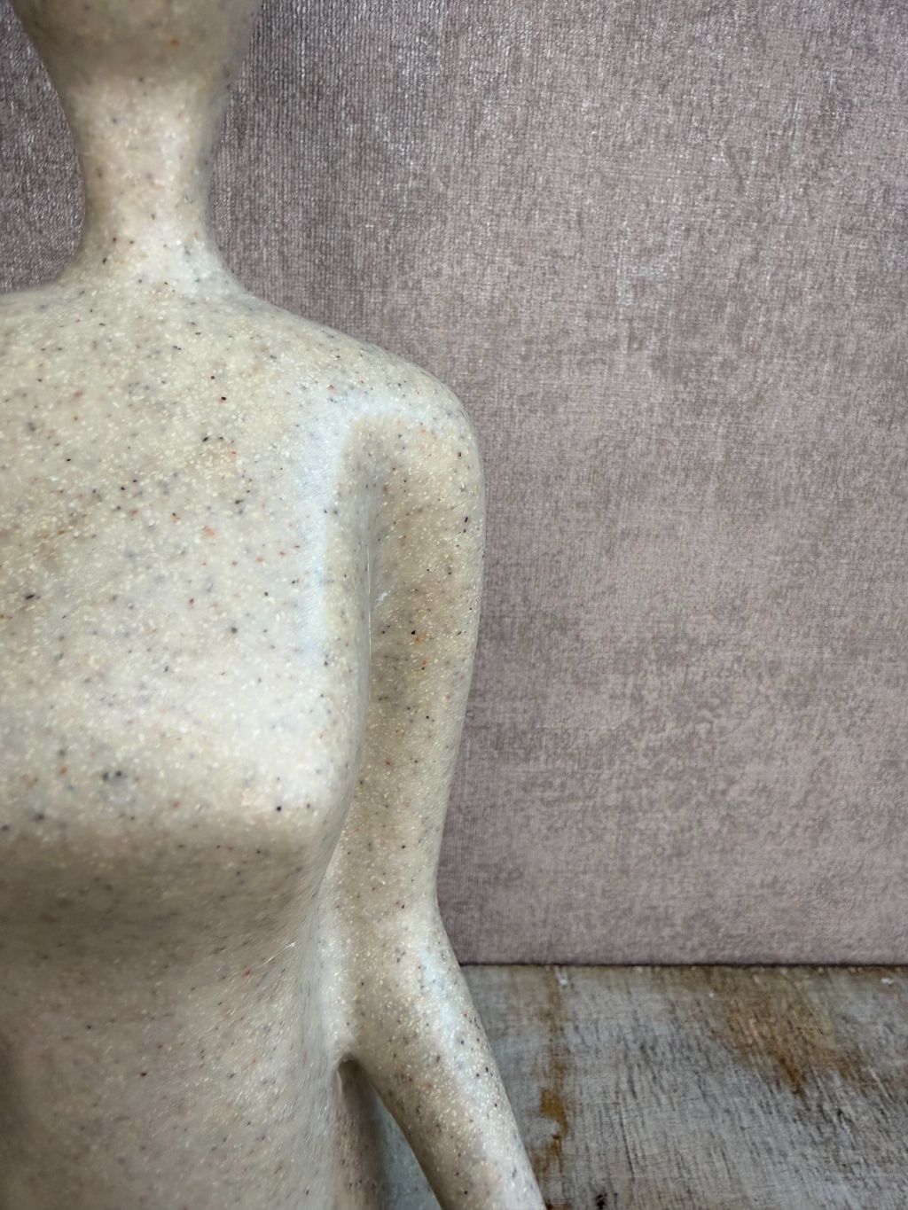 Ornament van een zittend figuur in lotuspositie in beige-grijze kleur op een houten ondergrond.