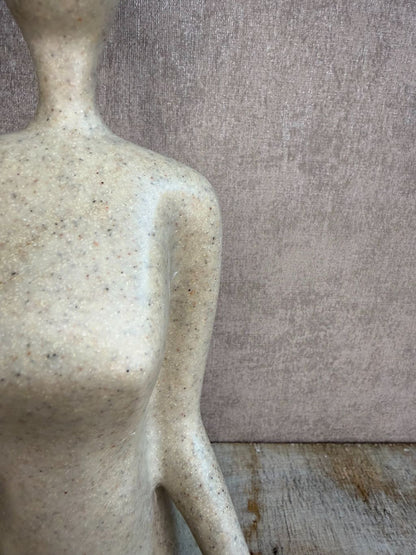 Ornament van een zittend figuur in lotuspositie in beige-grijze kleur op een houten ondergrond.