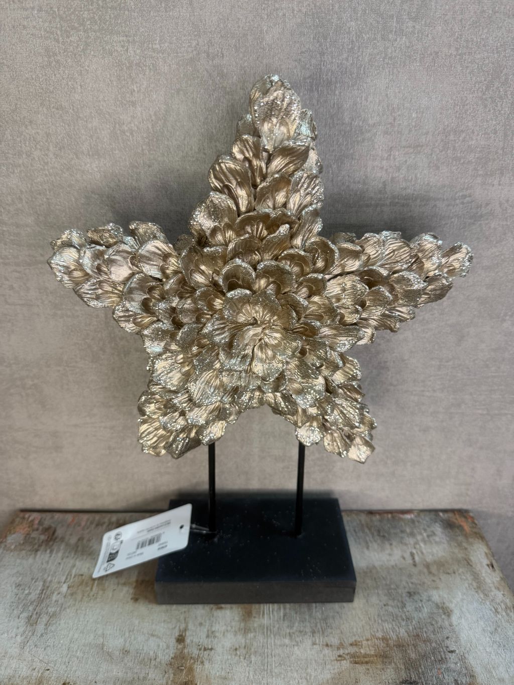 Ornament Ster glitter champagne – decoratieve ster met glanzende bloemvormige blaadjes op zwarte standaard.