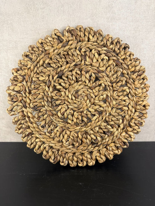 Ronde handgemaakte placemat van grof gevlochten raffia in warme bruintinten met decoratieve rand.