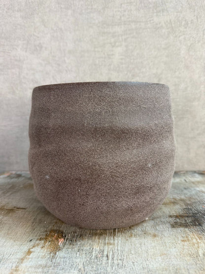 Ronde bruine keramieken plantenpot met matte structuur op een houten ondergrond.