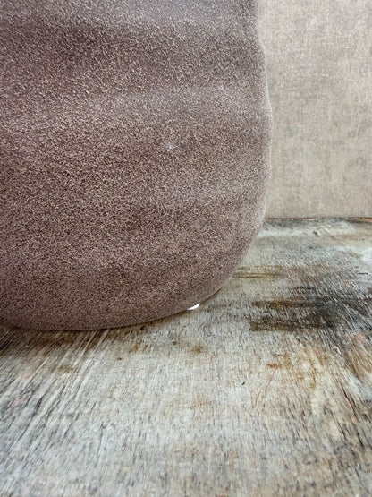 Ronde bruine keramieken plantenpot met matte structuur op een houten ondergrond.