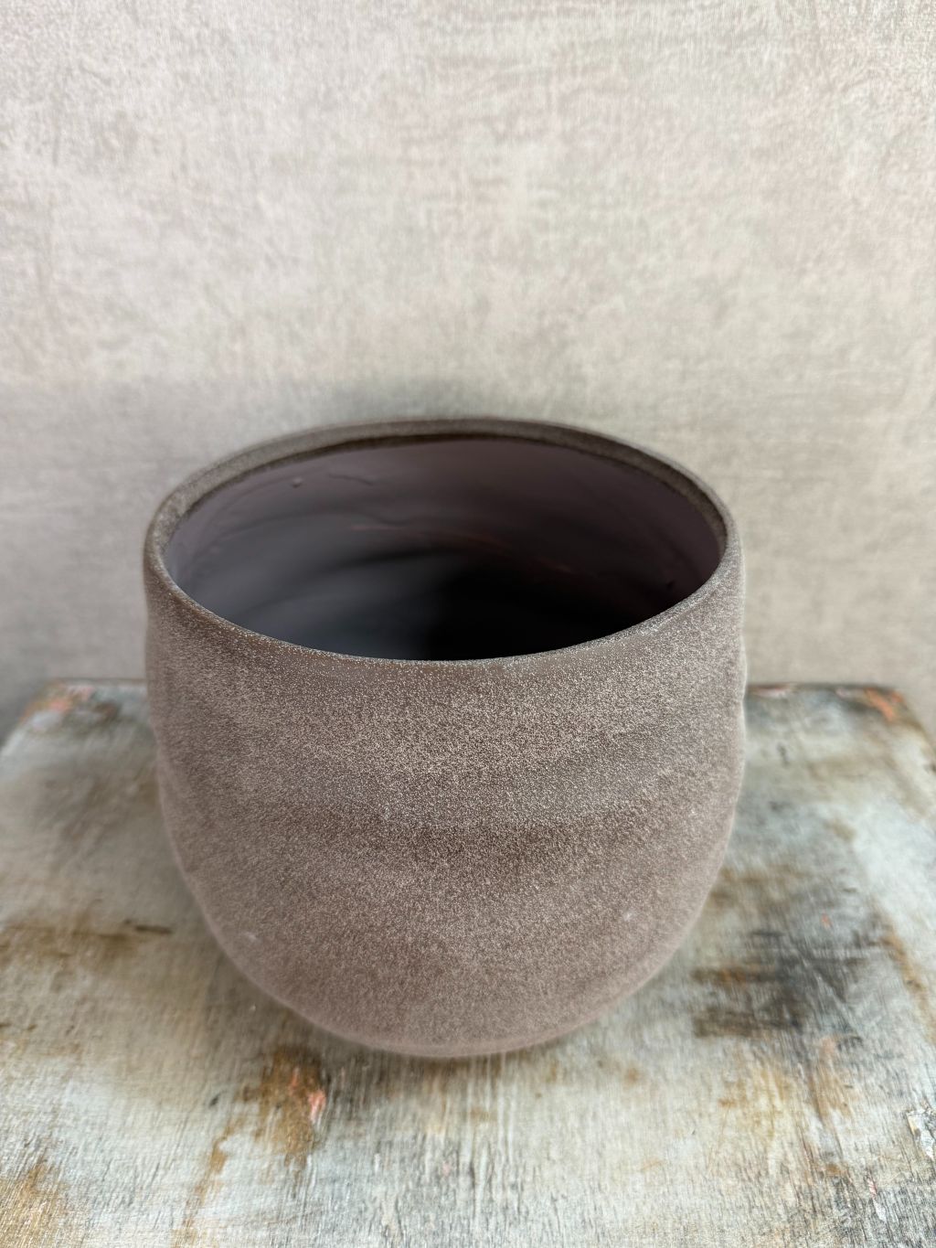 Ronde bruine keramieken plantenpot met matte structuur op een houten ondergrond.