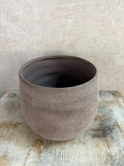 Ronde bruine keramieken plantenpot met matte structuur op een houten ondergrond.