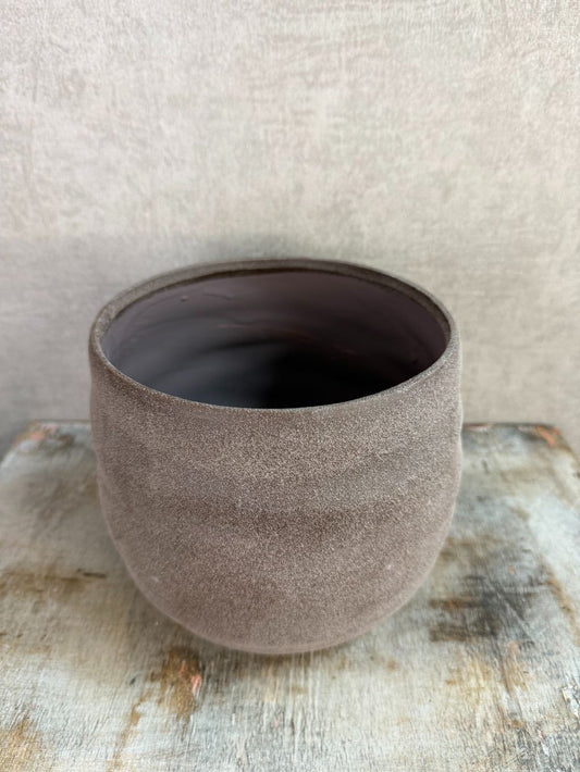 Ronde bruine keramieken plantenpot met matte structuur op een houten ondergrond.