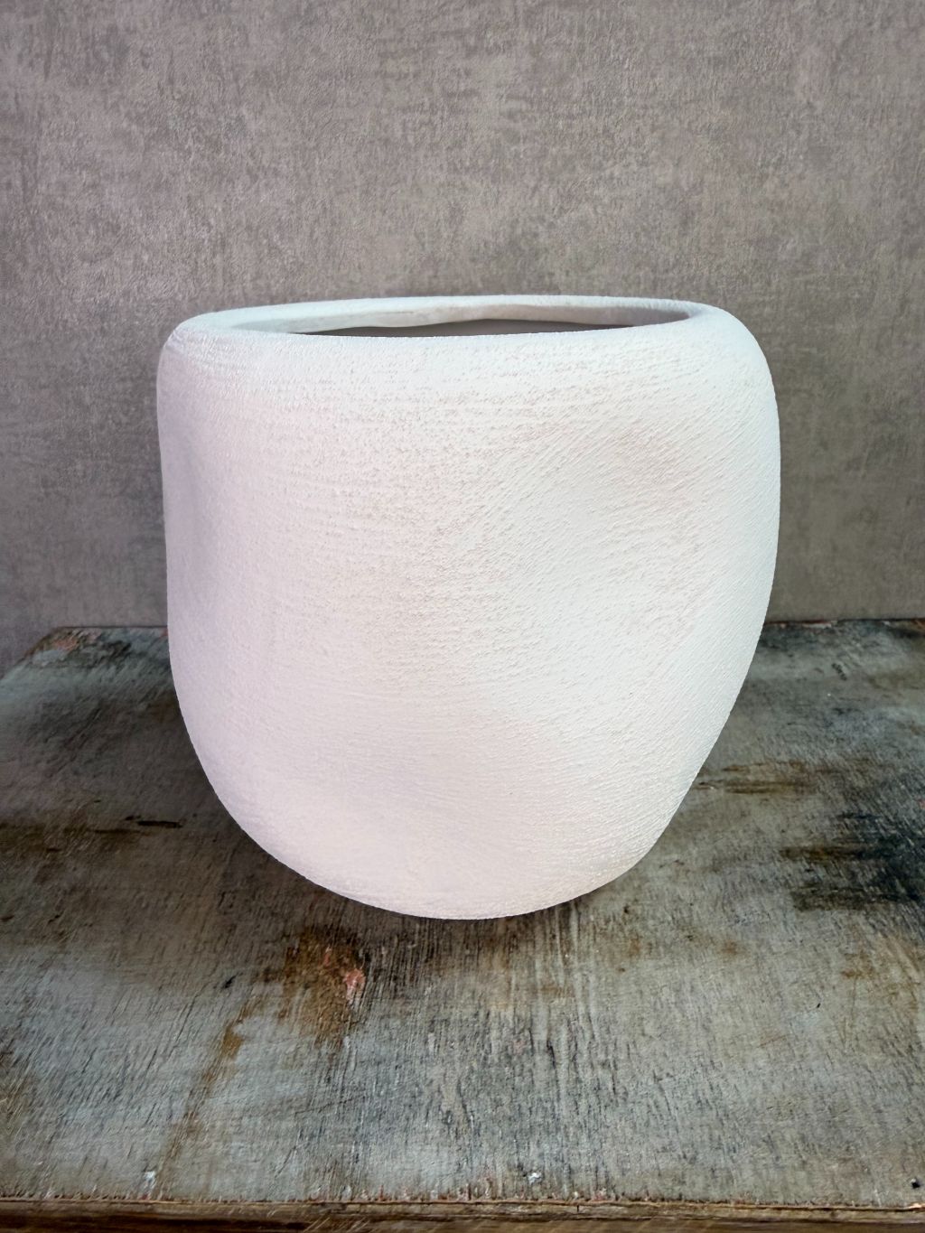 Witte keramieken plantenpot met ronde vorm en matte afwerking op een houten ondergrond.