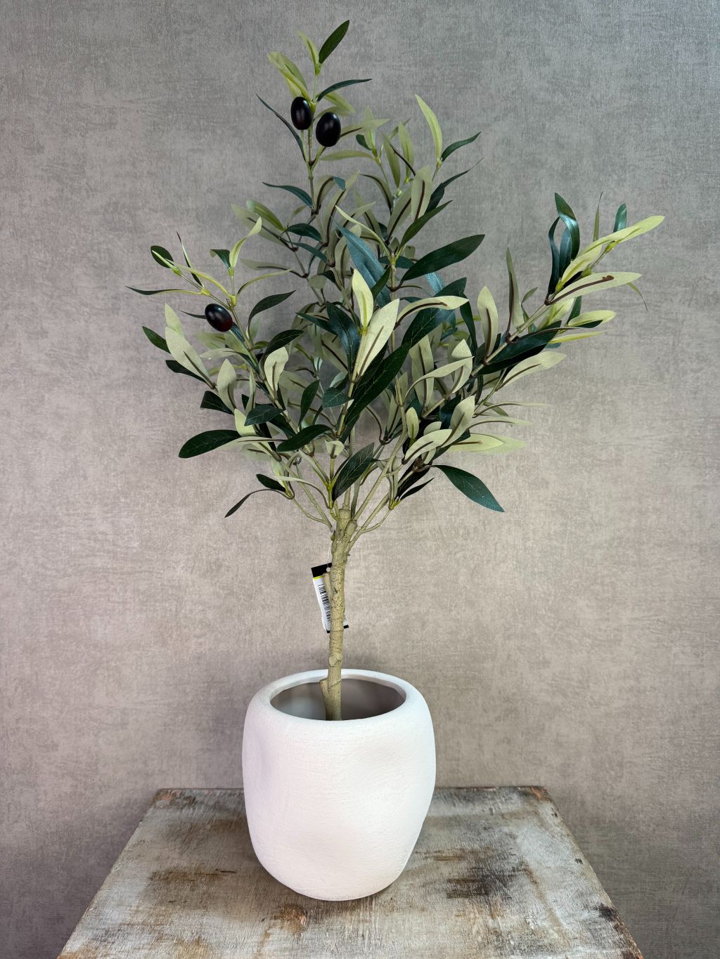 Witte keramieken plantenpot met ronde vorm, een kunst olijfboompje en matte afwerking op een houten ondergrond.