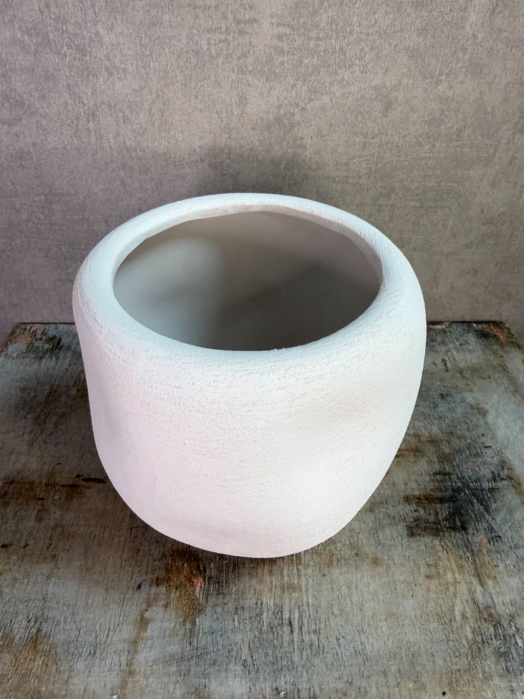 Witte keramieken plantenpot met ronde vorm en matte afwerking op een houten ondergrond.