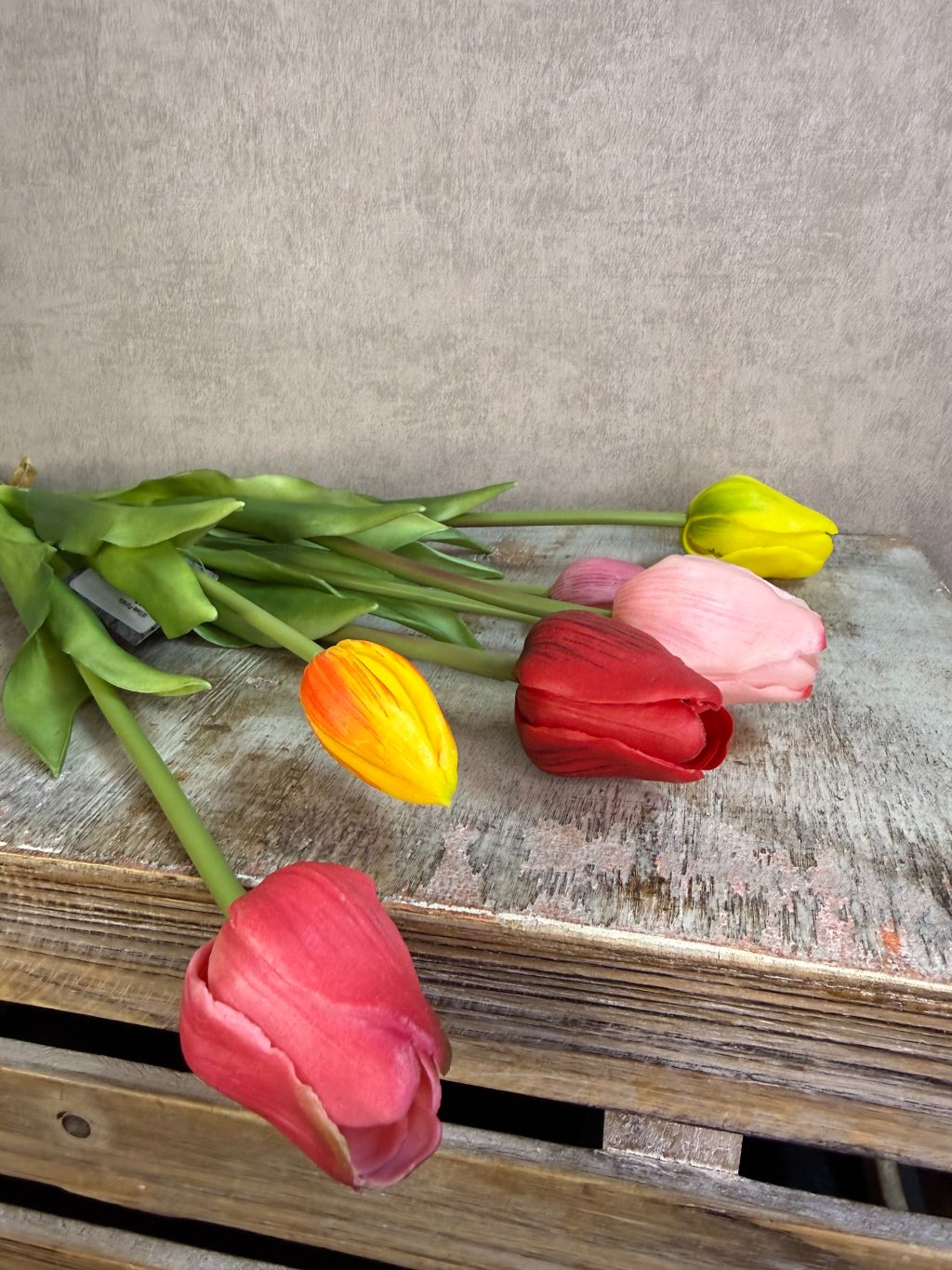 Bos real touch tulpen in een bonte mix van kleuren met groene bladeren, staand op een houten ondergrond tegen een neutrale achtergrond.