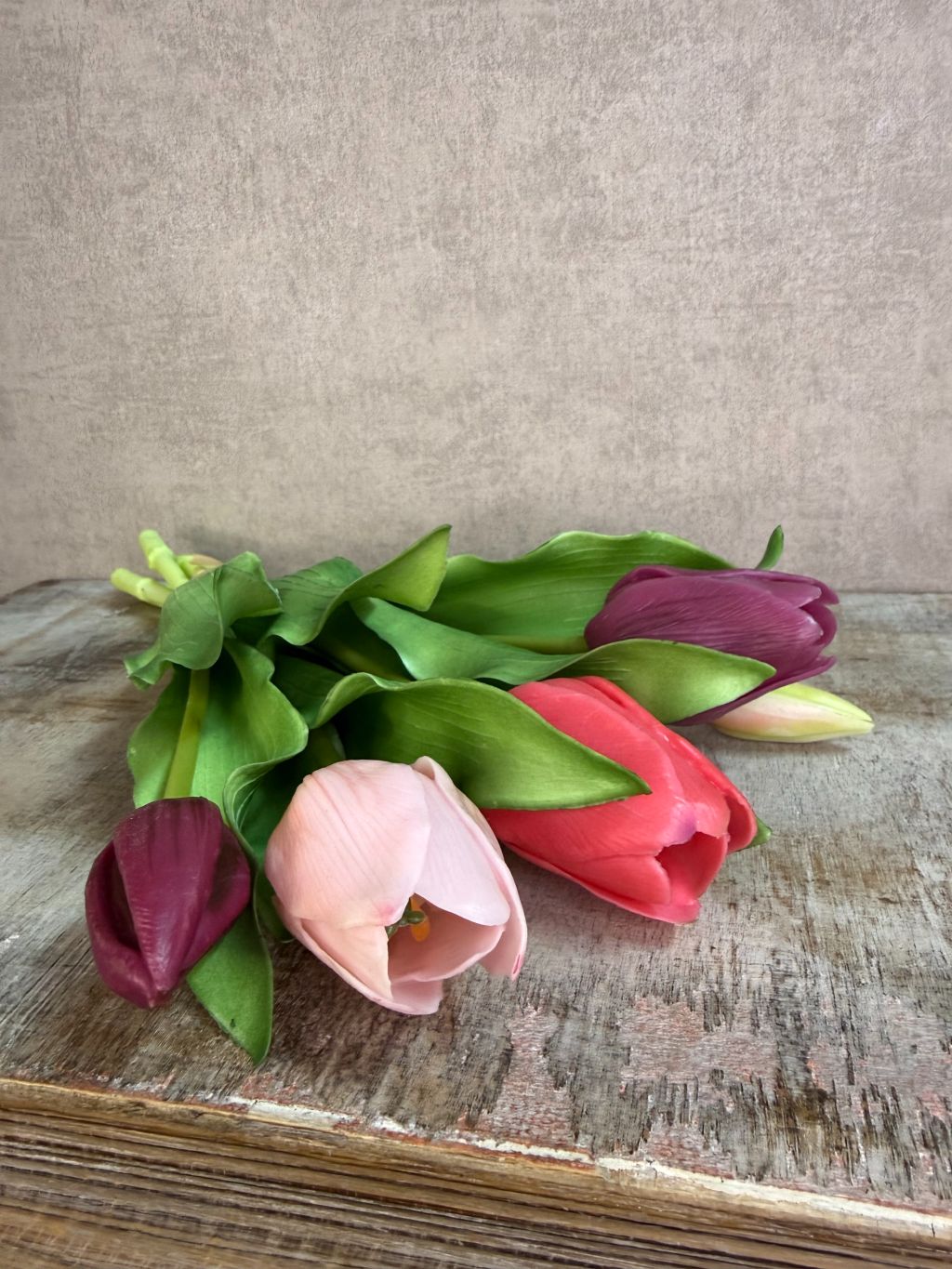 Bos real touch tulpen in paars- en rozetinten met groene bladeren, liggend op een houten ondergrond tegen een neutrale achtergrond.