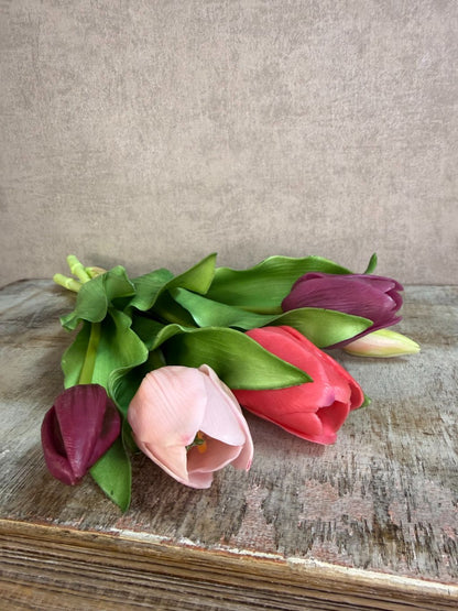 Bos real touch tulpen in paars- en rozetinten met groene bladeren, liggend op een houten ondergrond tegen een neutrale achtergrond.