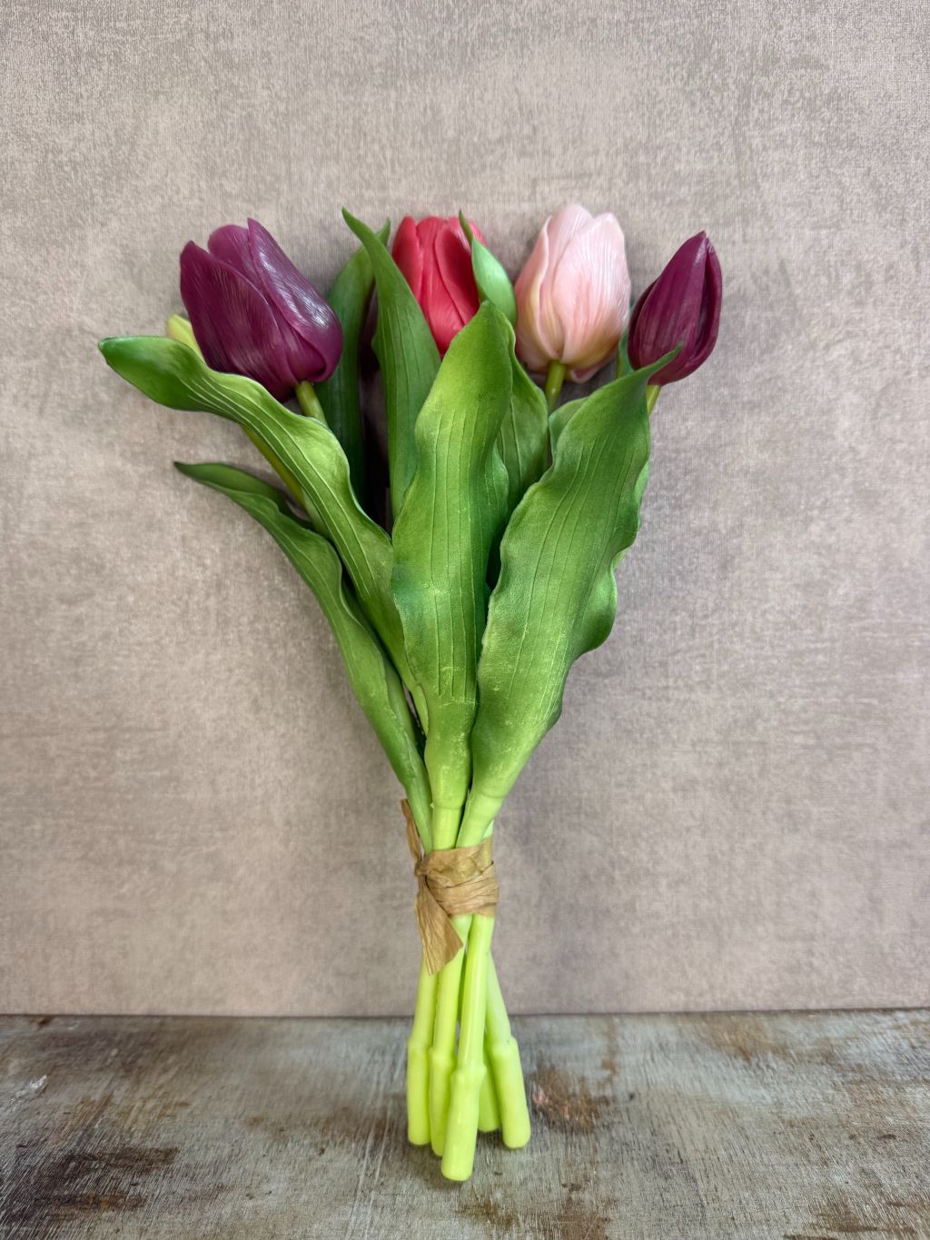 Bos real touch tulpen in paars- en rozetinten met groene bladeren, liggend op een houten ondergrond tegen een neutrale achtergrond.