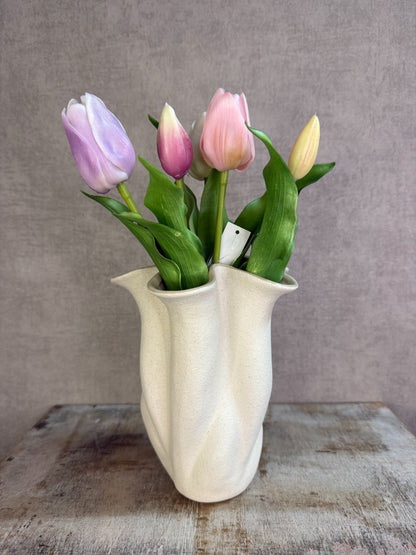Bos real touch tulpen in zachte pasteltinten met groene bladeren, staand op een houten ondergrond tegen een neutrale achtergrond.