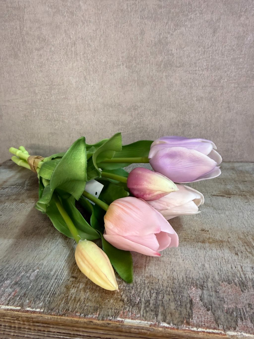 Bos real touch tulpen in zachte pasteltinten met groene bladeren, staand op een houten ondergrond tegen een neutrale achtergrond.