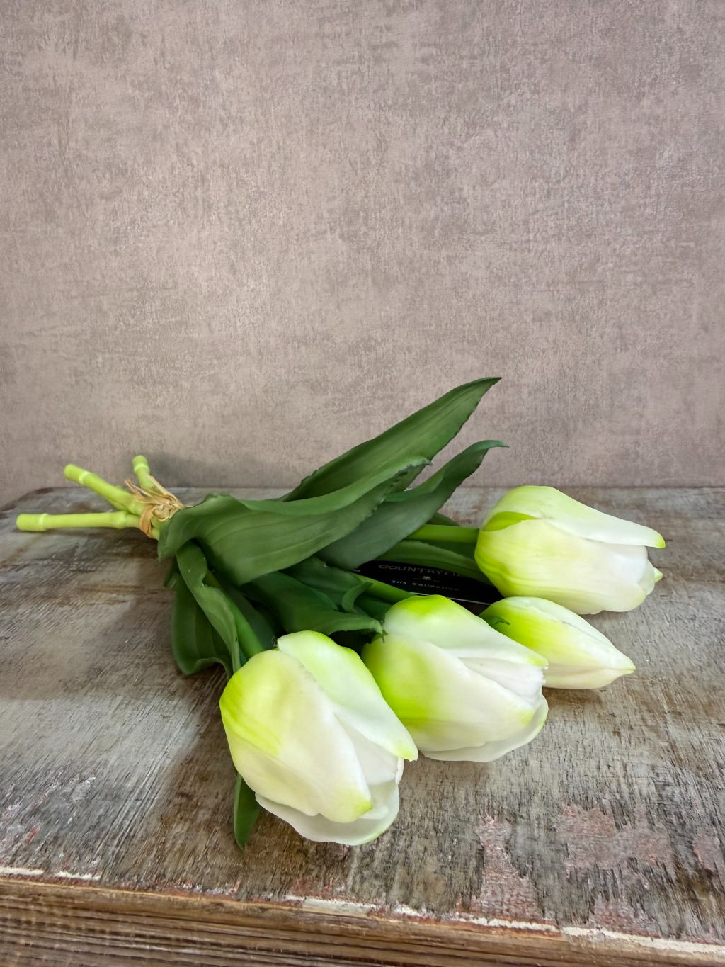 Bos real touch tulpen in wit met groene bladeren, samengebonden en geplaatst tegen een neutrale achtergrond.