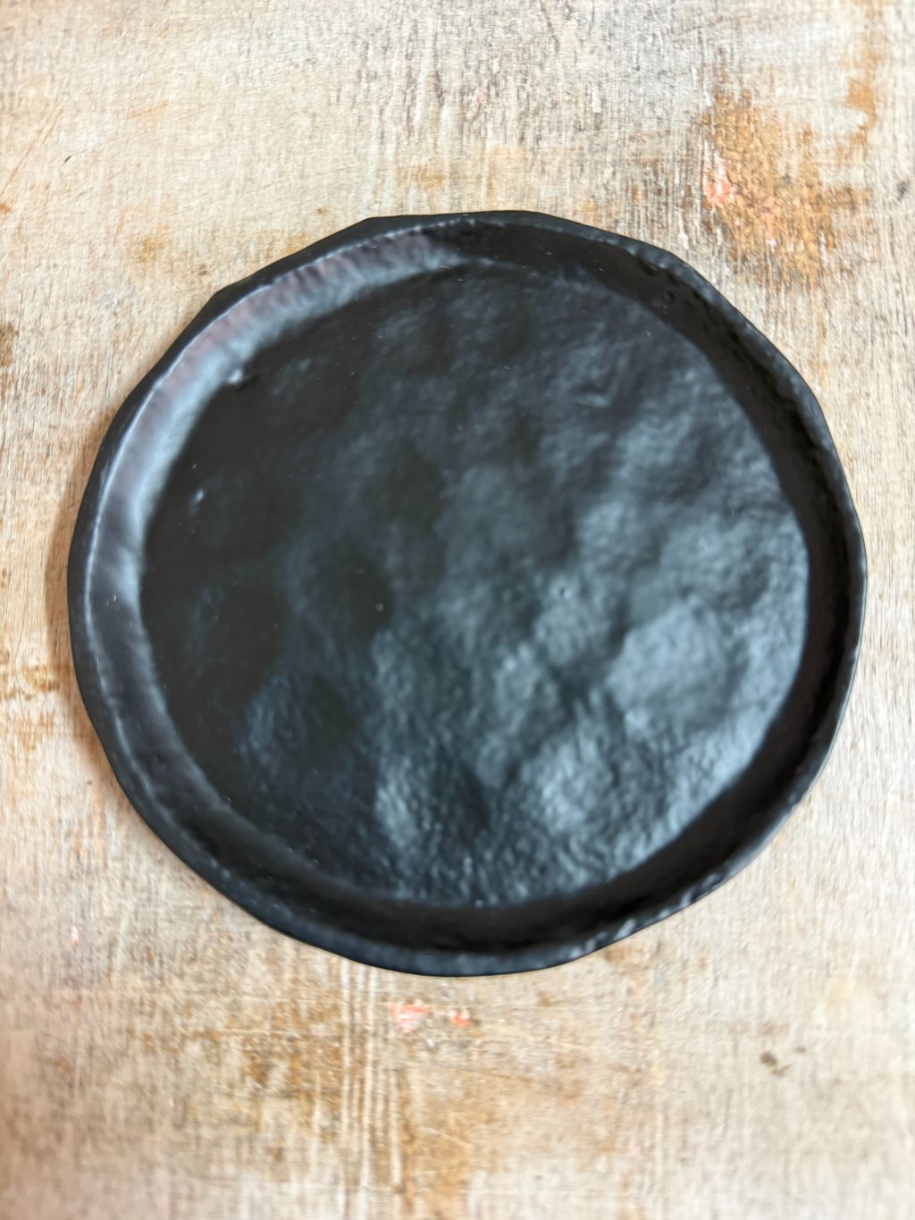 Rond zwart metalen schaaltje Forley met subtiel oneffen oppervlak, geplaatst op een houten ondergrond.