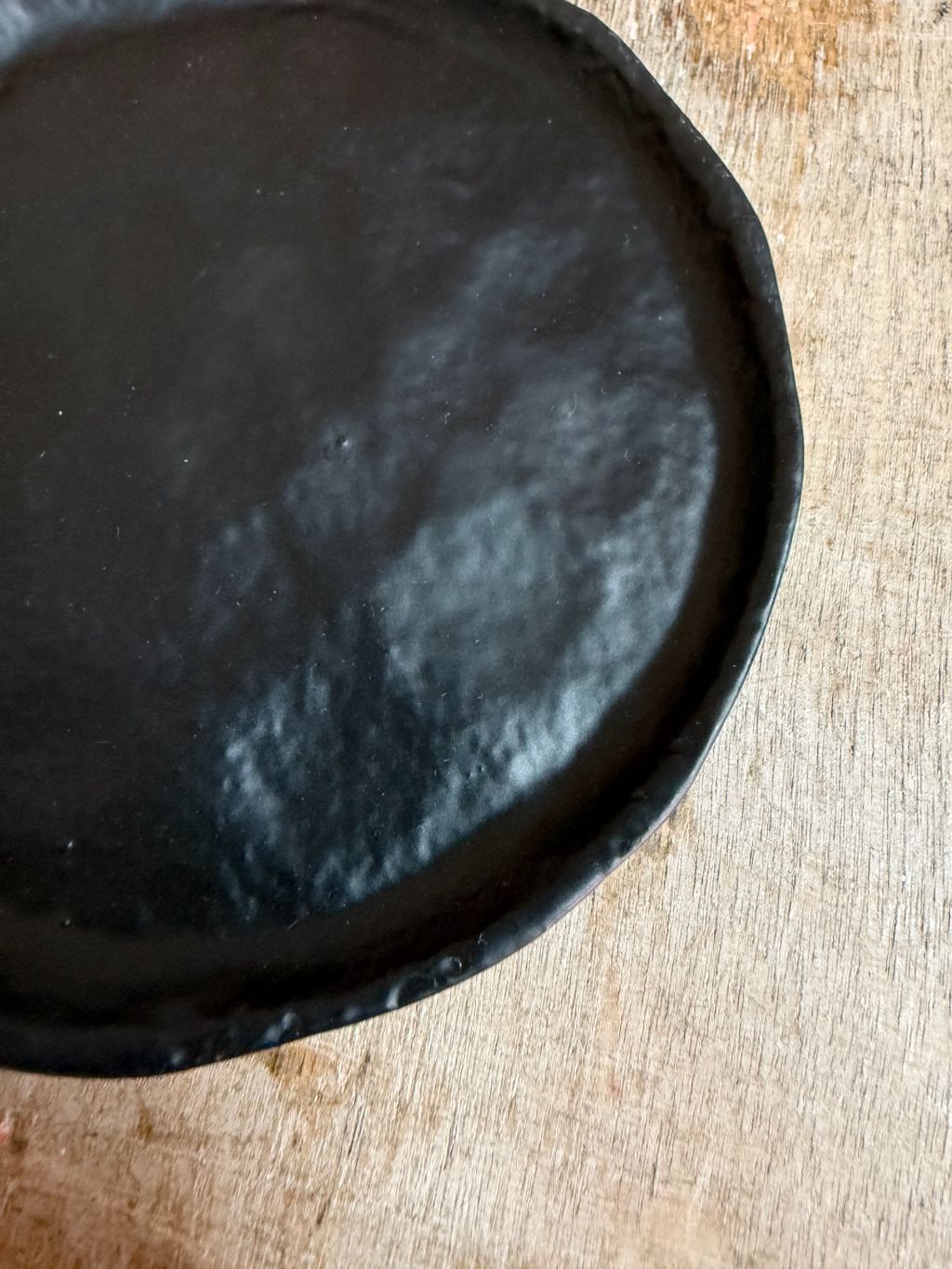 Rond zwart metalen schaaltje Forley met subtiel oneffen oppervlak, geplaatst op een houten ondergrond.