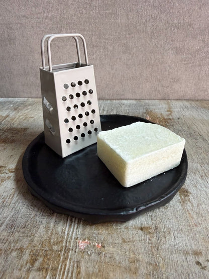 Rond zwart metalen schaaltje Forley met subtiel oneffen oppervlak, geplaatst op een houten ondergrond. met een rasp en amberblokje