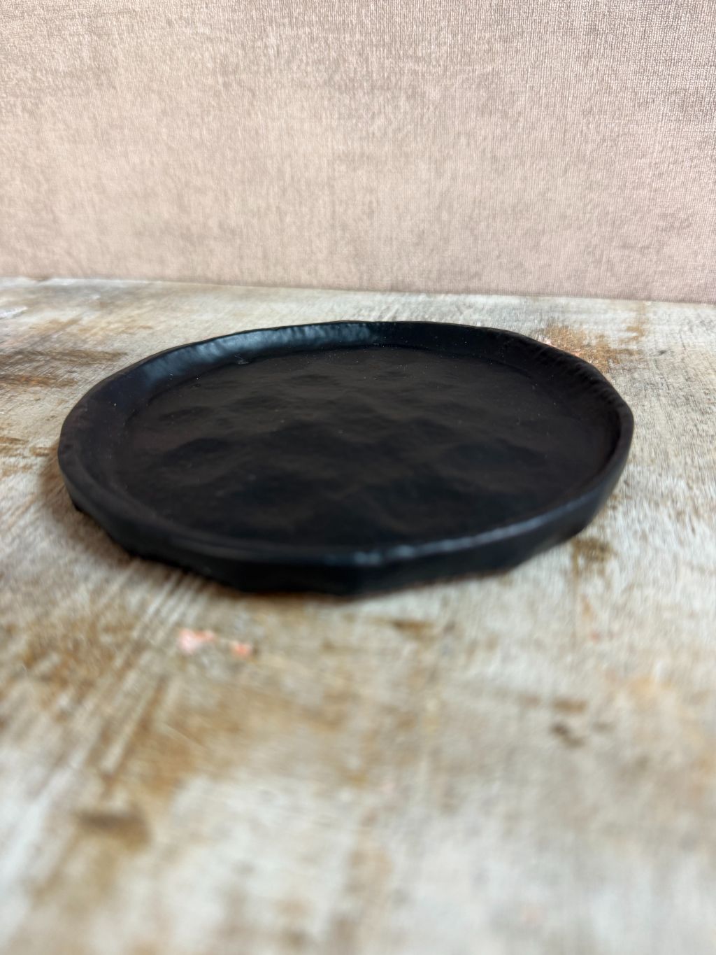 Rond zwart metalen schaaltje Forley met subtiel oneffen oppervlak, geplaatst op een houten ondergrond.