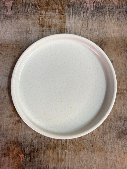 Wit keramieken schaaltje met opstaande rand op een houten ondergrond tegen een neutrale achtergrond.