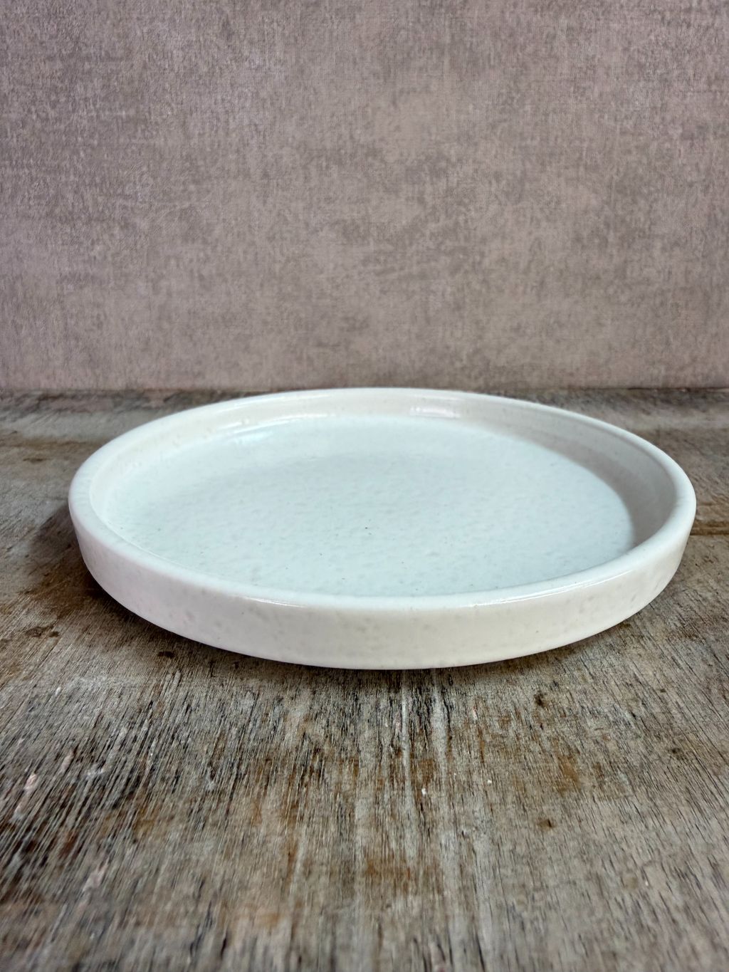 Wit keramieken schaaltje met opstaande rand op een houten ondergrond tegen een neutrale achtergrond.