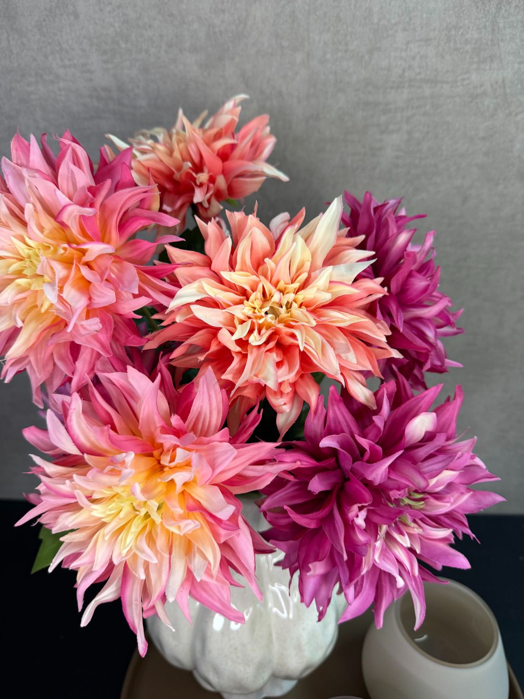 Tafel decoratie set met beige vaas, roze en perzikkleurige bloemen en twee waxinelichthouders op een rond bruin dienblad.