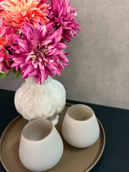 Tafel decoratie set met beige vaas, roze en perzikkleurige bloemen en twee waxinelichthouders op een rond bruin dienblad.