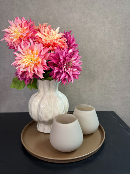 Tafel decoratie set met beige vaas, roze en perzikkleurige bloemen en twee waxinelichthouders op een rond bruin dienblad.