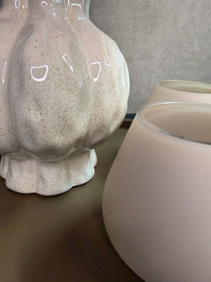 Tafel decoratie set met beige vaas, roze en perzikkleurige bloemen en twee waxinelichthouders op een rond bruin dienblad.