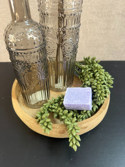 Decoratieset op houten dienblad met glazen flessen, lavendelkleurige kunstbloemen, amberblokje en kunstgroen.