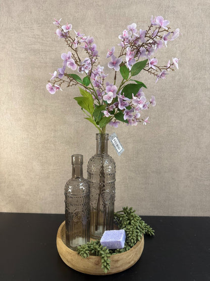 Decoratieset op houten dienblad met glazen flessen, lavendelkleurige kunstbloemen, amberblokje en kunstgroen.