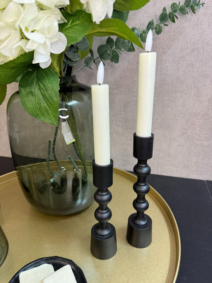 Goudkleurig dienblad met vaas met witte hortensia’s en eucalyptus, zwarte kandelaars, glazen waxinelichthouders en amberblokjes.