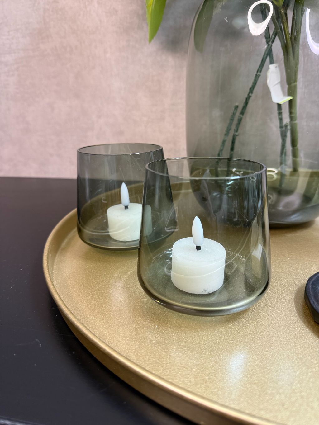 Goudkleurig dienblad met vaas met witte hortensia’s en eucalyptus, zwarte kandelaars, glazen waxinelichthouders en amberblokjes.