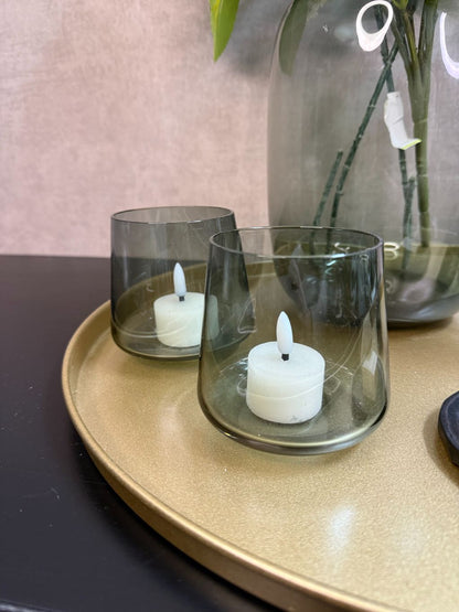 Goudkleurig dienblad met vaas met witte hortensia’s en eucalyptus, zwarte kandelaars, glazen waxinelichthouders en amberblokjes.