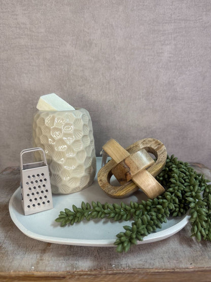 Tafel decoratieset met beige keramische houder, houten decoratie, amberblokje en groen takje op ovaal dienblad.