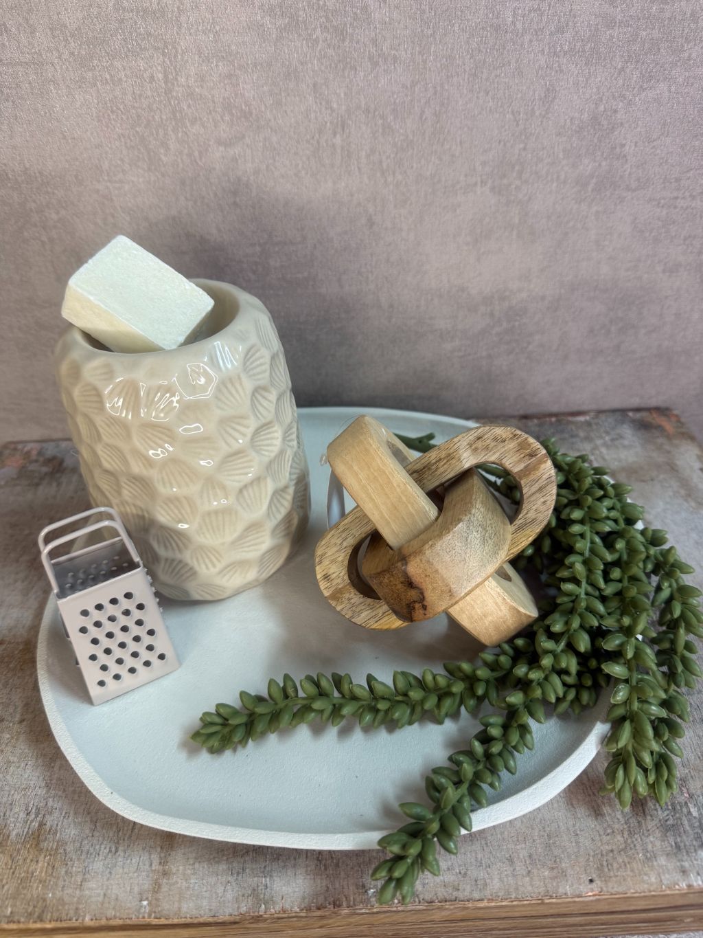 Tafel decoratieset met beige keramische houder, houten decoratie, amberblokje en groen takje op ovaal dienblad.