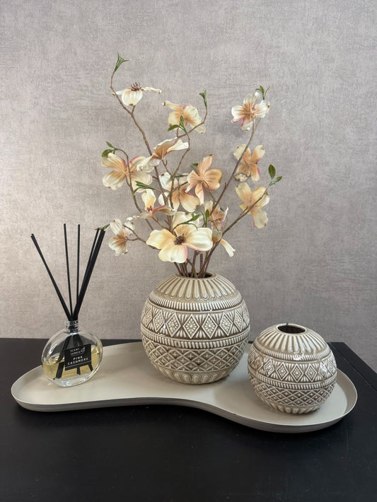 Beige tafel decoratieset met keramieken bollenvaasjes, crèmekleurige kunstbloemen, geurstokjes en een beige dienblad op een zwarte tafel.