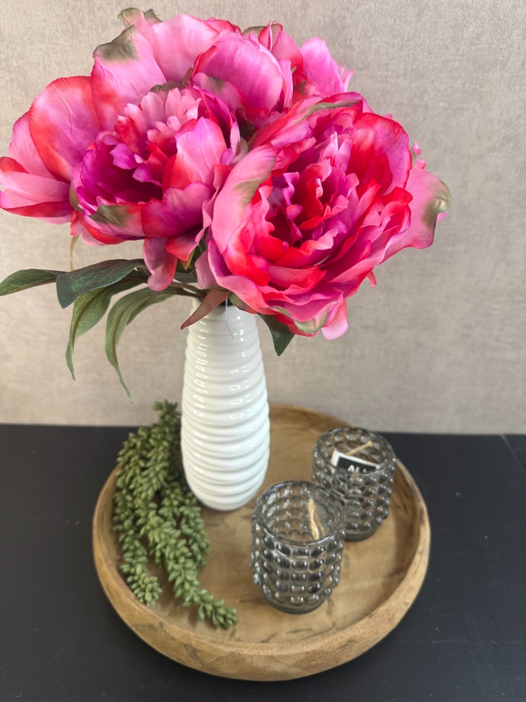 Decoratieset met roze pioenrozen in witte vaas op houten dienblad, aangevuld met zwarte theelichthouders en een groene kunst erwtenplant.