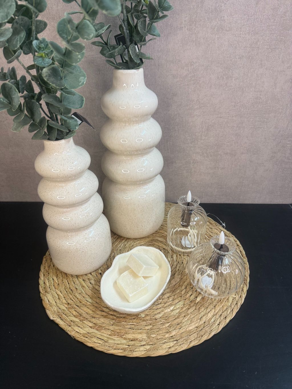 Tafel decoratie set Lovi – beige vazen met eucalyptus­takken, LED-oliekaarsjes en amberblokjes op gevlochten placemat.