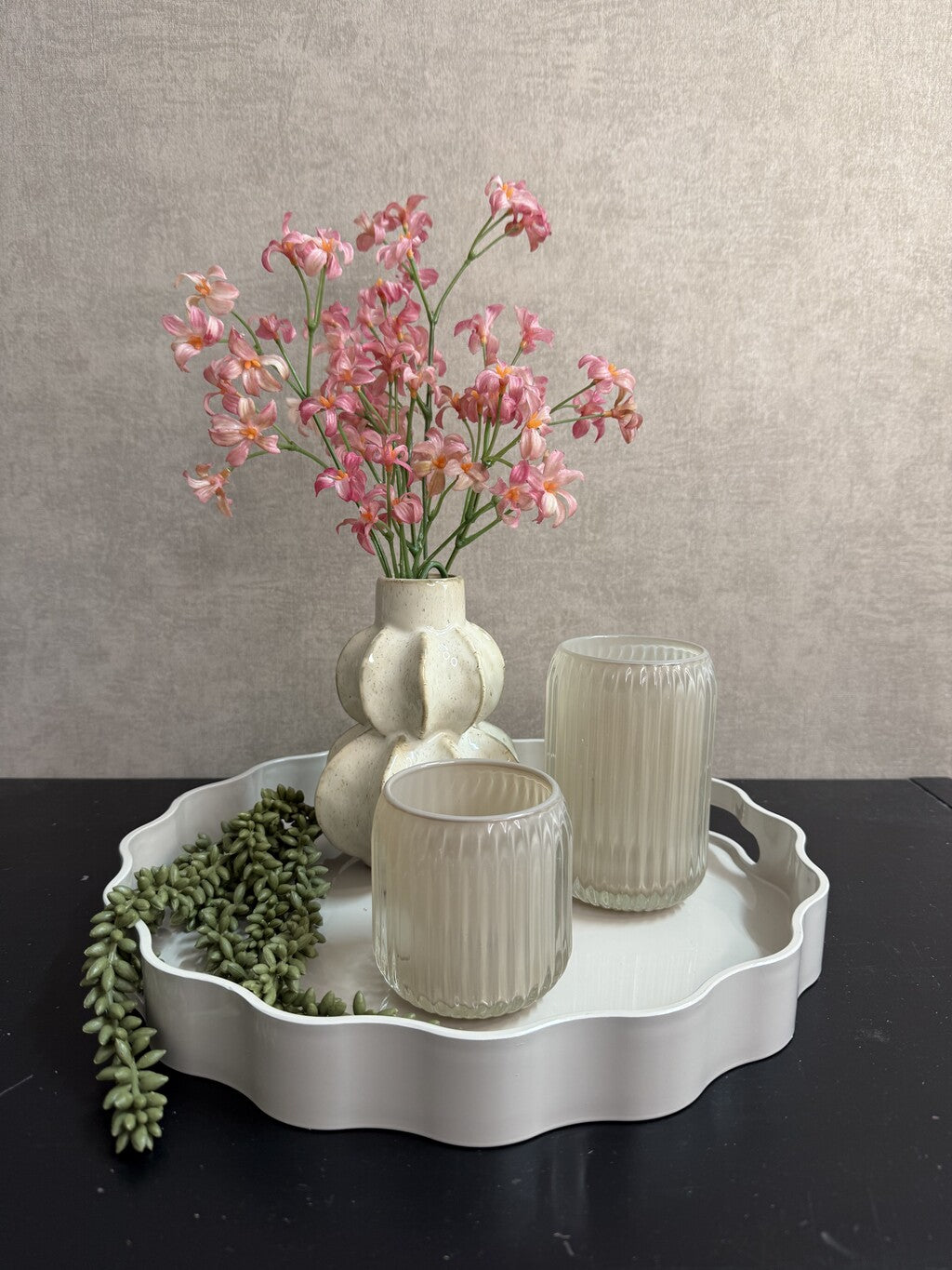 Tafel decoratie set Lulu met rond beige dienblad, vaas met roze bloemen, groene hangplant en twee glazen houders.