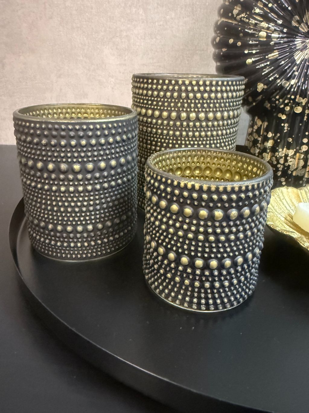 Tafel decoratie set Nelle – zwarte vaas met witte bloemen, goudkleurige schaal met amberblokjes en zwarte waxinelichthouders op rond dienblad.